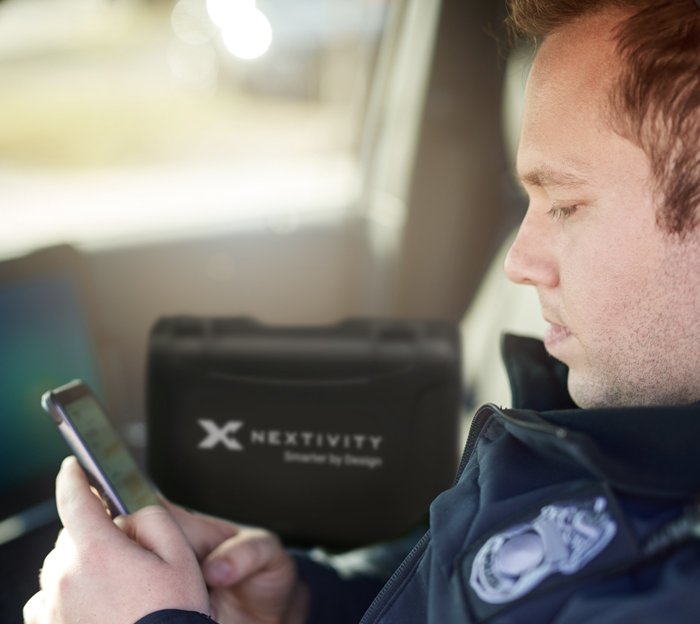 Police in car, looking at his mobile phone with Nextivity device in the background.
