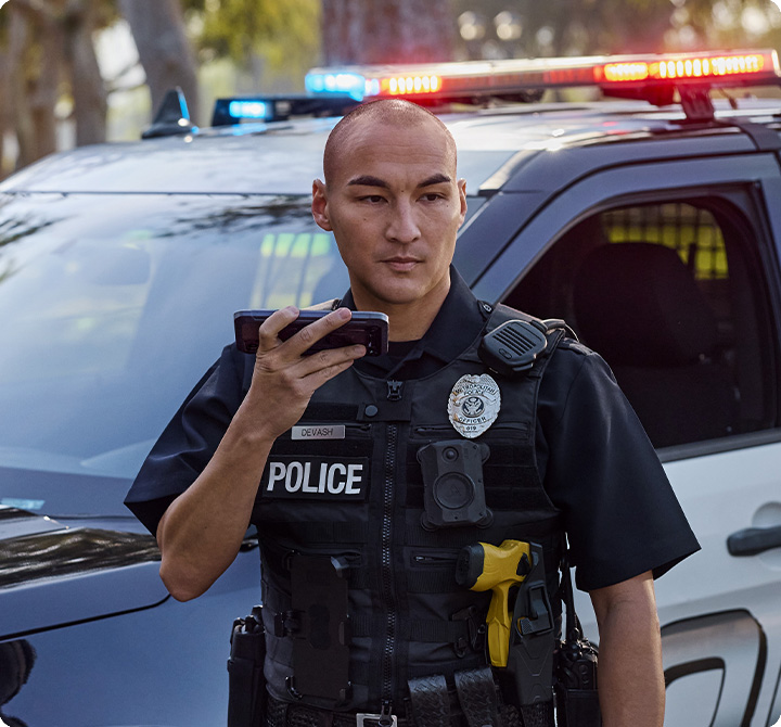 Two police officers standing outside patrol car, using FirstNet Push-to-Talk devices and FirstNet Fusion