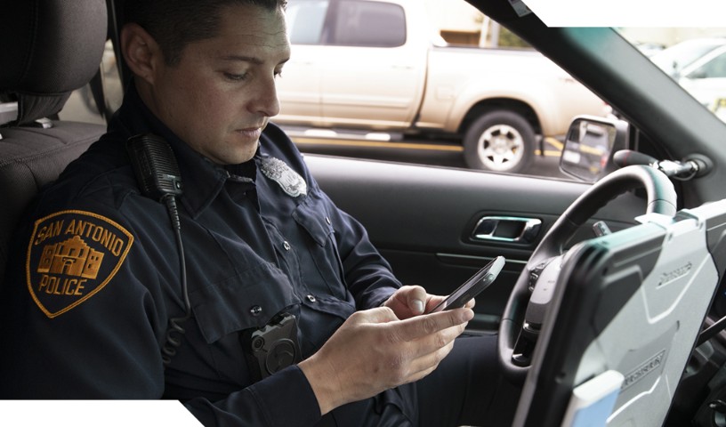 San Antonio policeman browses FirstNet communications on mobile device in vehicle.