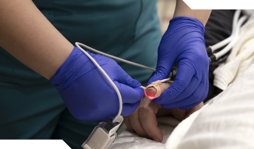 Close-up of nurse's hands in blue gloves checking Oxygen levels of patient using index finger.
