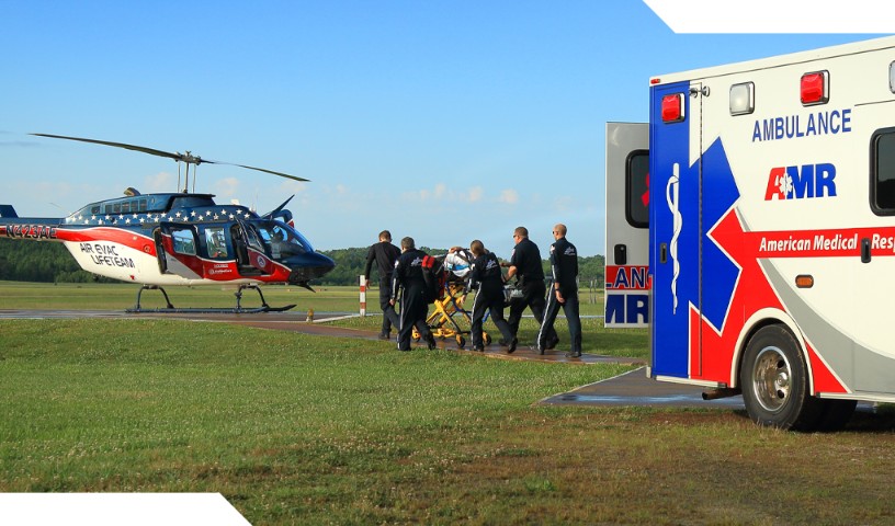 EMT transfers patient on bed to air evacuation helicopter in an open field.